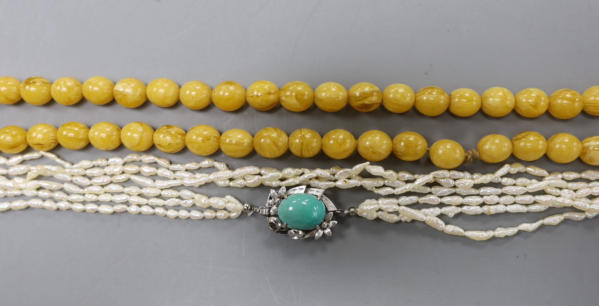 A multi-strand 'rice pearl' necklace with 18k white metal and turquoise set clasp, 66cm and an amber necklace.